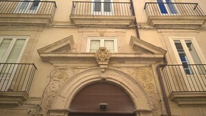 Fachada de edificio con una entrada central en arco, detalles de cantería y varios balcones con barandillas de metal.