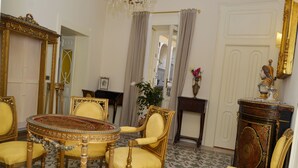 Una habitación con una mesa redonda rodeada por cuatro sillas, un espejo, una mesita con un jarrón y un aparador con una estatua.