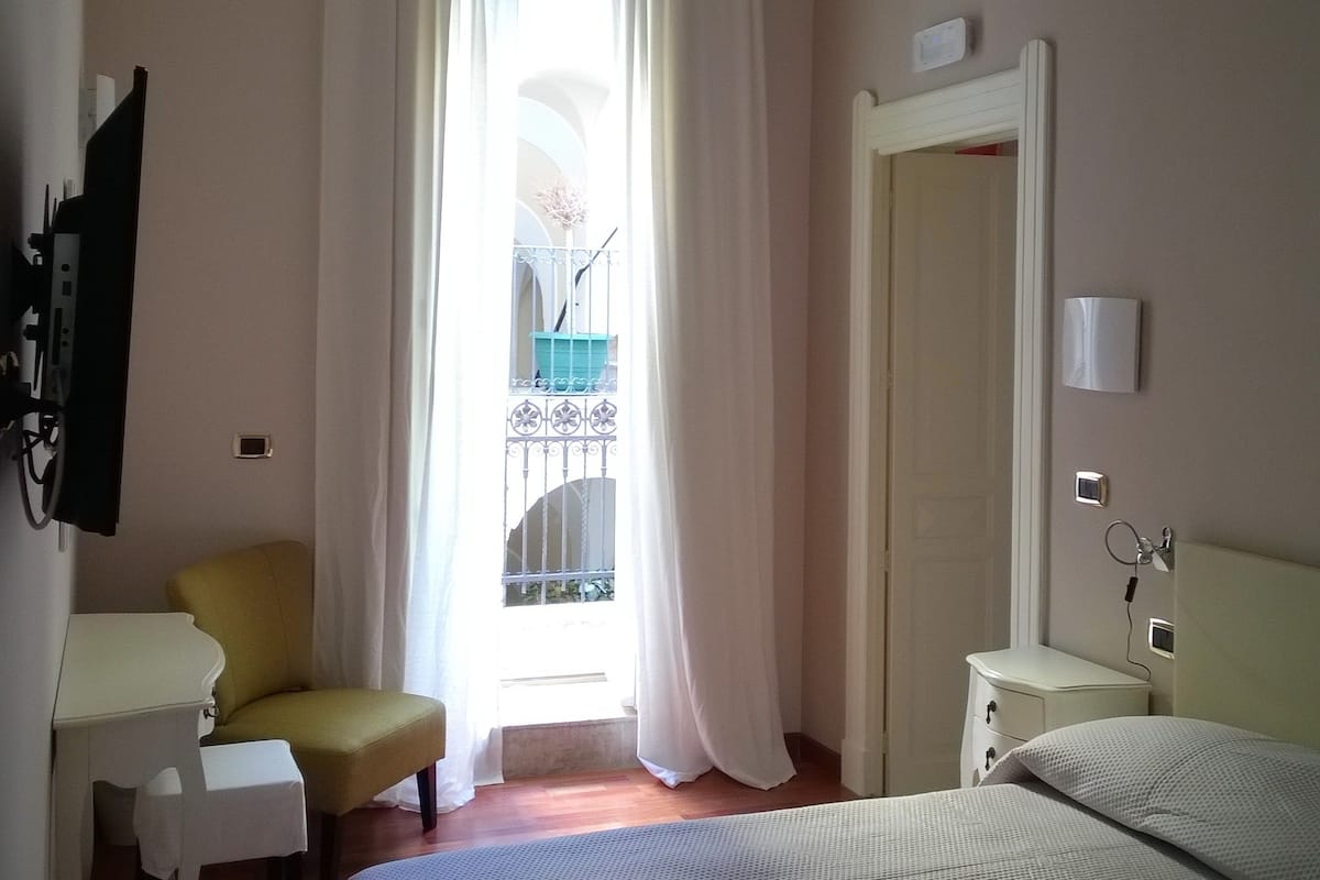 A hotel room with a bed, a chair, a desk, and a window with curtains.