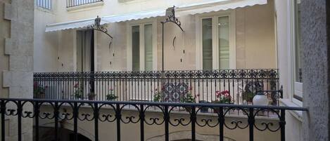 A courtyard with a balcony, a wrought iron railing, and potted plants.