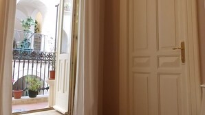 Una habitación con piso de madera, una puerta blanca y un ventanal con cortinas.