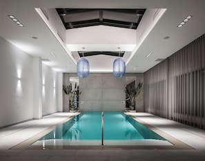 Uma piscina interior moderna com vista clara do teto, das paredes e de uma grande janela à direita.