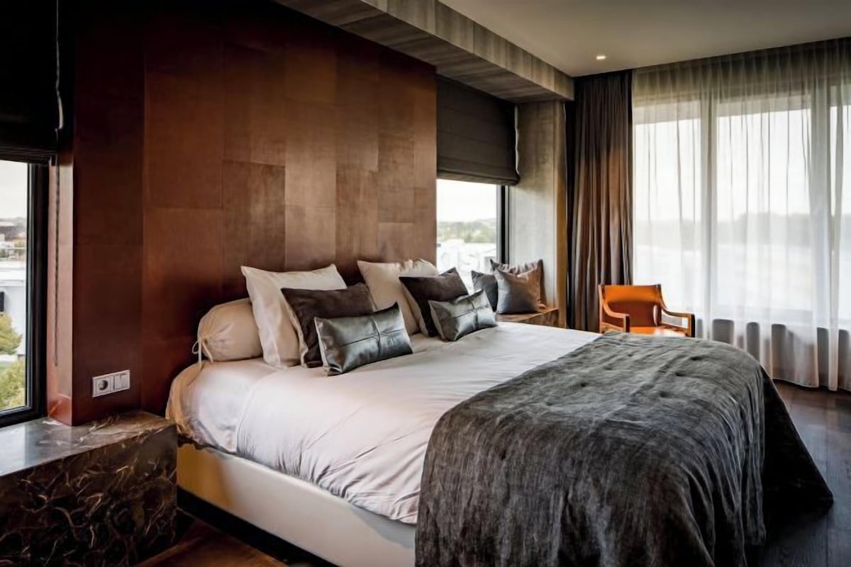 Un dormitorio moderno con una cama grande, cabecera de madera y vistas al exterior.