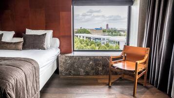 Ein Hotelzimmer mit einem Bett, einem Sessel, einem Fenster mit Blick auf die Stadt und einer Wand mit Marmorelementen.