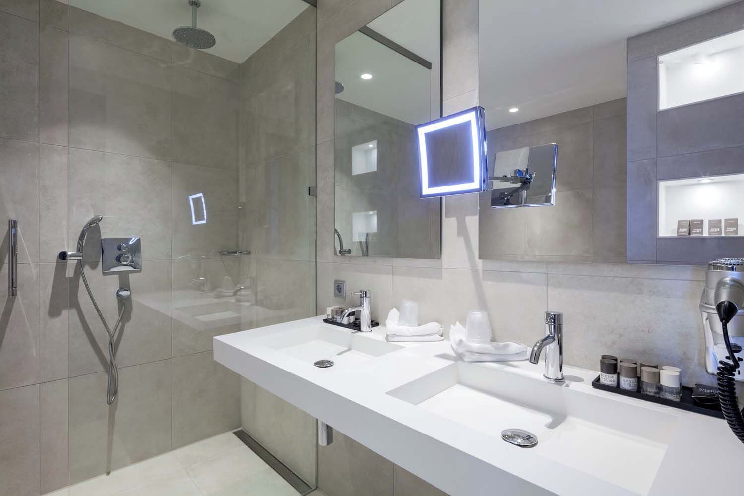 A modern bathroom with two sinks, a shower, and a large mirror.