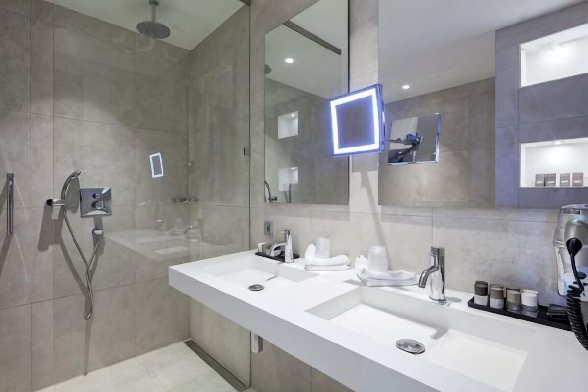 Een moderne badkamer met een grote spiegel, twee wastafels, een douche en een handdoekhouder.