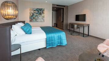 A hotel room with a bed, a desk, a chair, a TV, and a wall art piece.