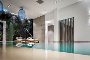 Un área de piscina interior moderna con sillones de descanso, un gran mural en la pared y una ventana alta y estrecha.