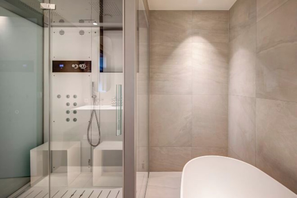 A modern bathroom with a glass-enclosed shower, a white bathtub, and a tiled wall.