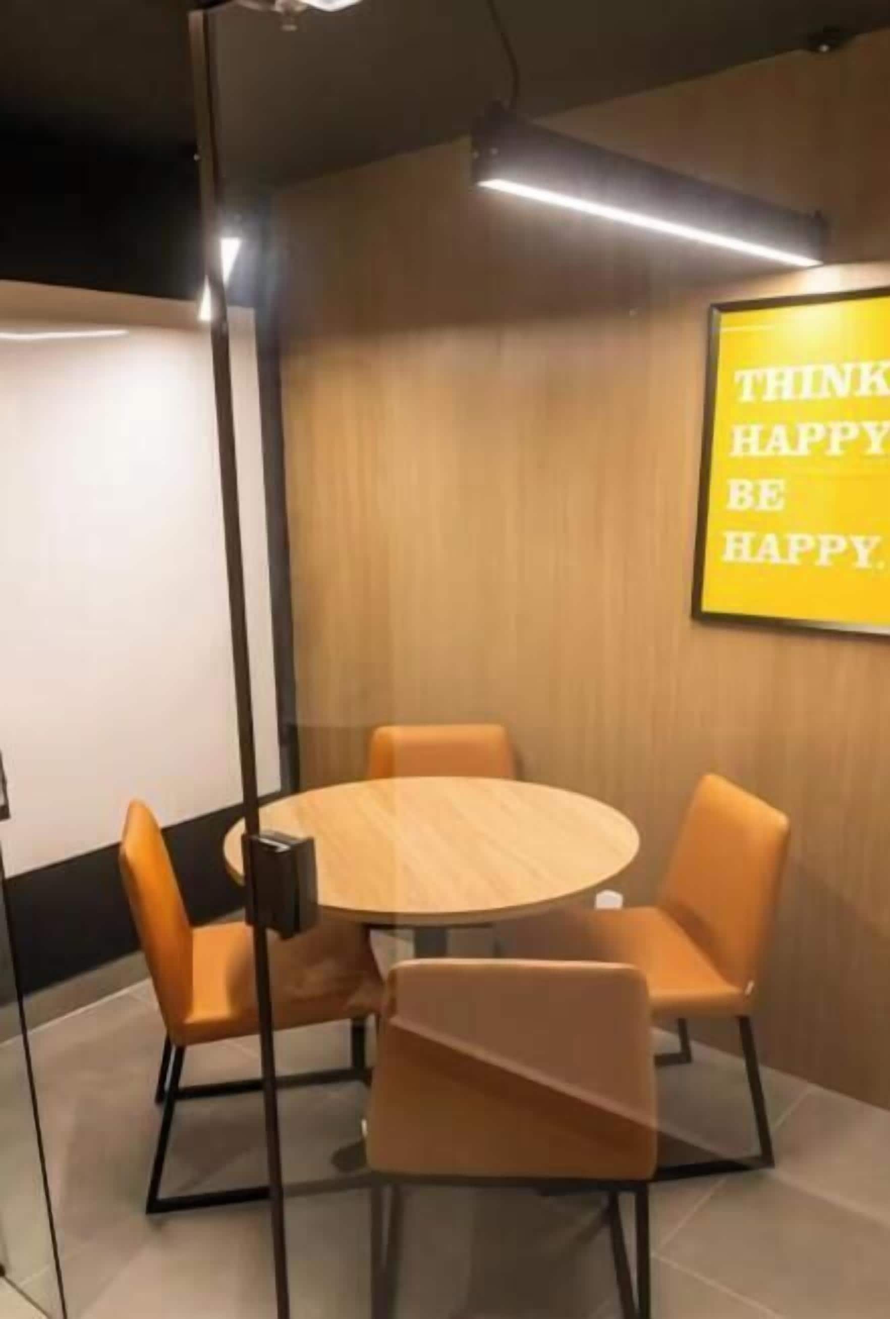 A conference room with a round table and four chairs, a motivational quote on the wall, and a glass partition.