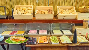 A buffet with various food items including bread, pastries, fruits, and cheeses. - Icarai Suites (Niteroi)