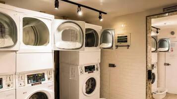 A laundry facility with multiple washing machines and dryers, a fire extinguisher, and a sign indicating maintenance.