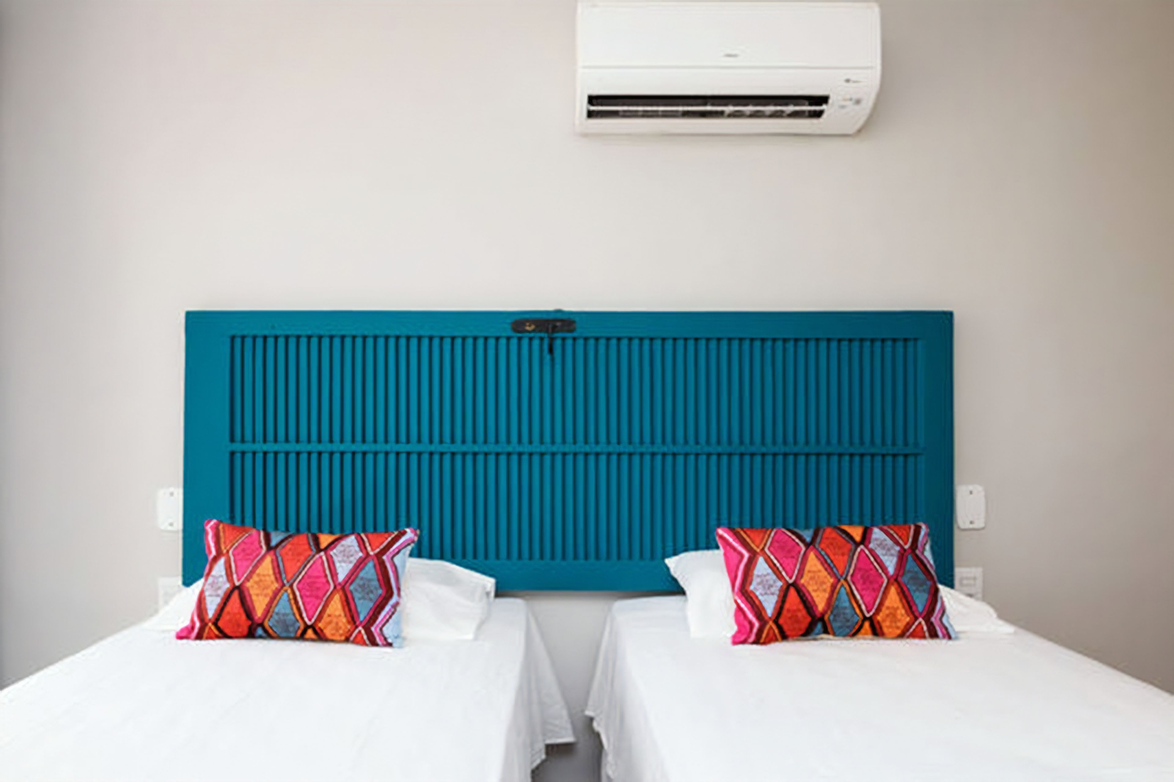 A hotel room with two beds, a teal headboard, and a white air conditioner above.