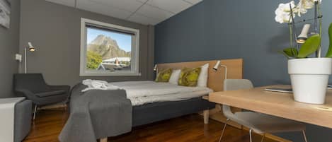Un dormitorio moderno con cama, escritorio y silla. Se ve una ventana con vista a la montaña.