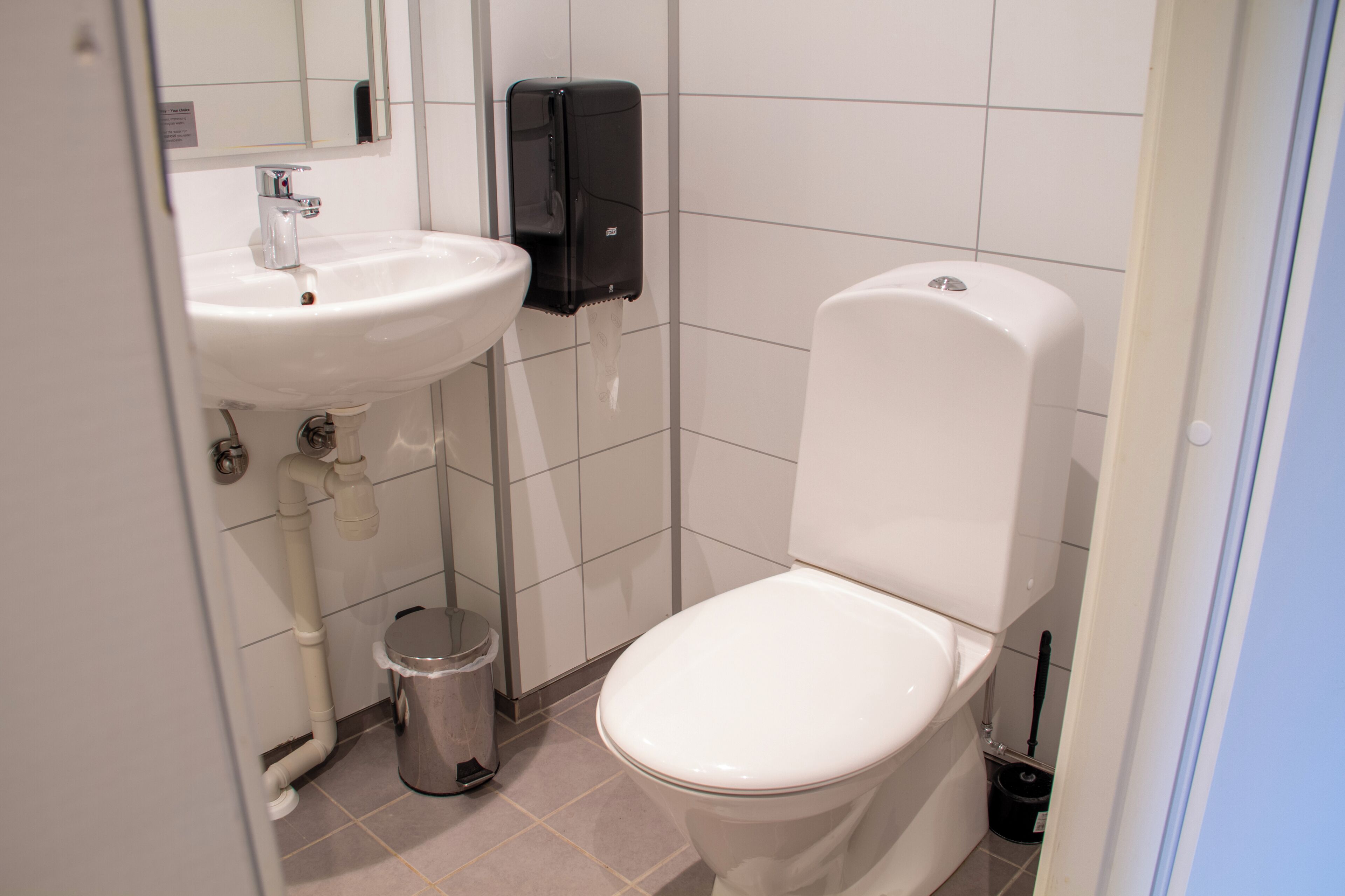 A bathroom with a white sink, a toilet, a trash can, and a hand dryer.