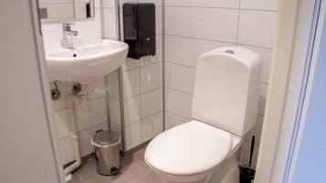 A bathroom with a white sink, a toilet, a trash can, and a hand dryer.