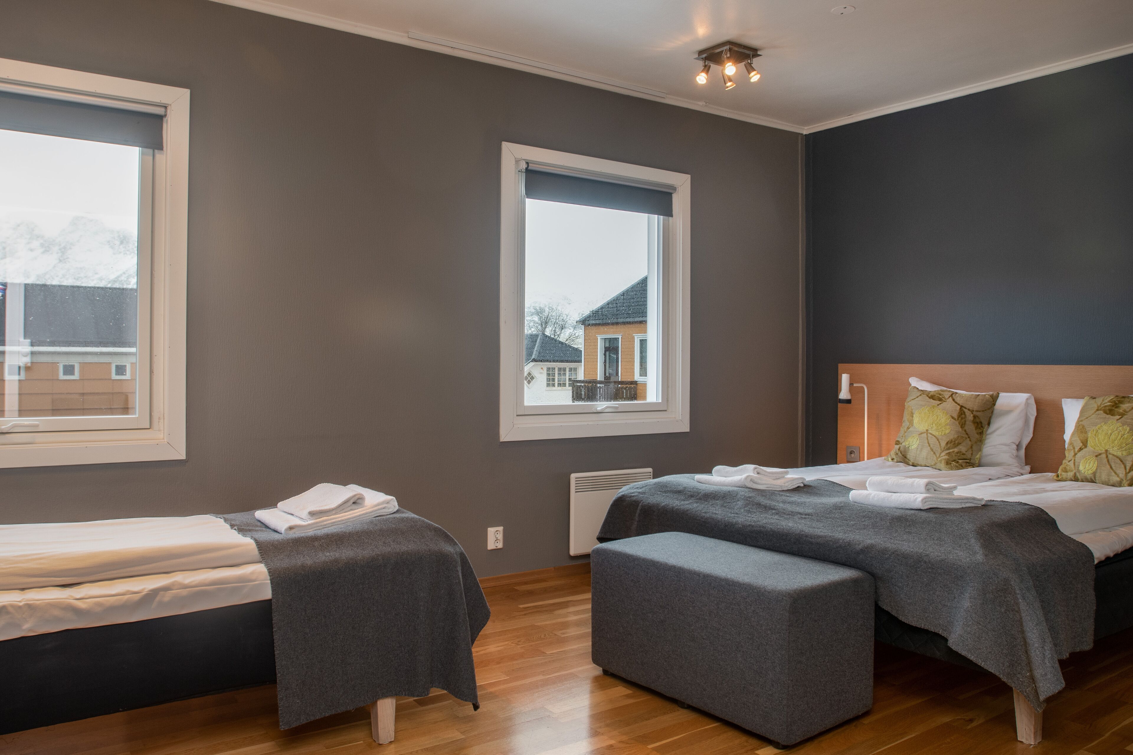 A modern hotel room with two single beds, a large window, and a view of a building outside.