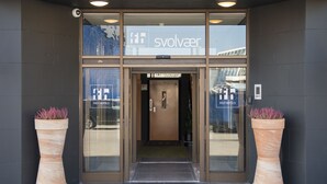 The entrance to a hotel with a modern design, featuring large glass doors and potted plants on either side.