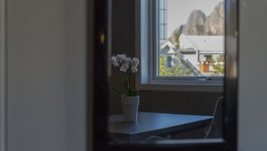 Una orquídea en maceta sobre una mesa junto a una ventana con vistas a edificios y montañas.