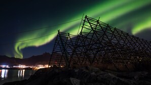 A nighttime view of a coastal area with a metal structure, possibly a bridge or pier, and the Northern Lights in the background.