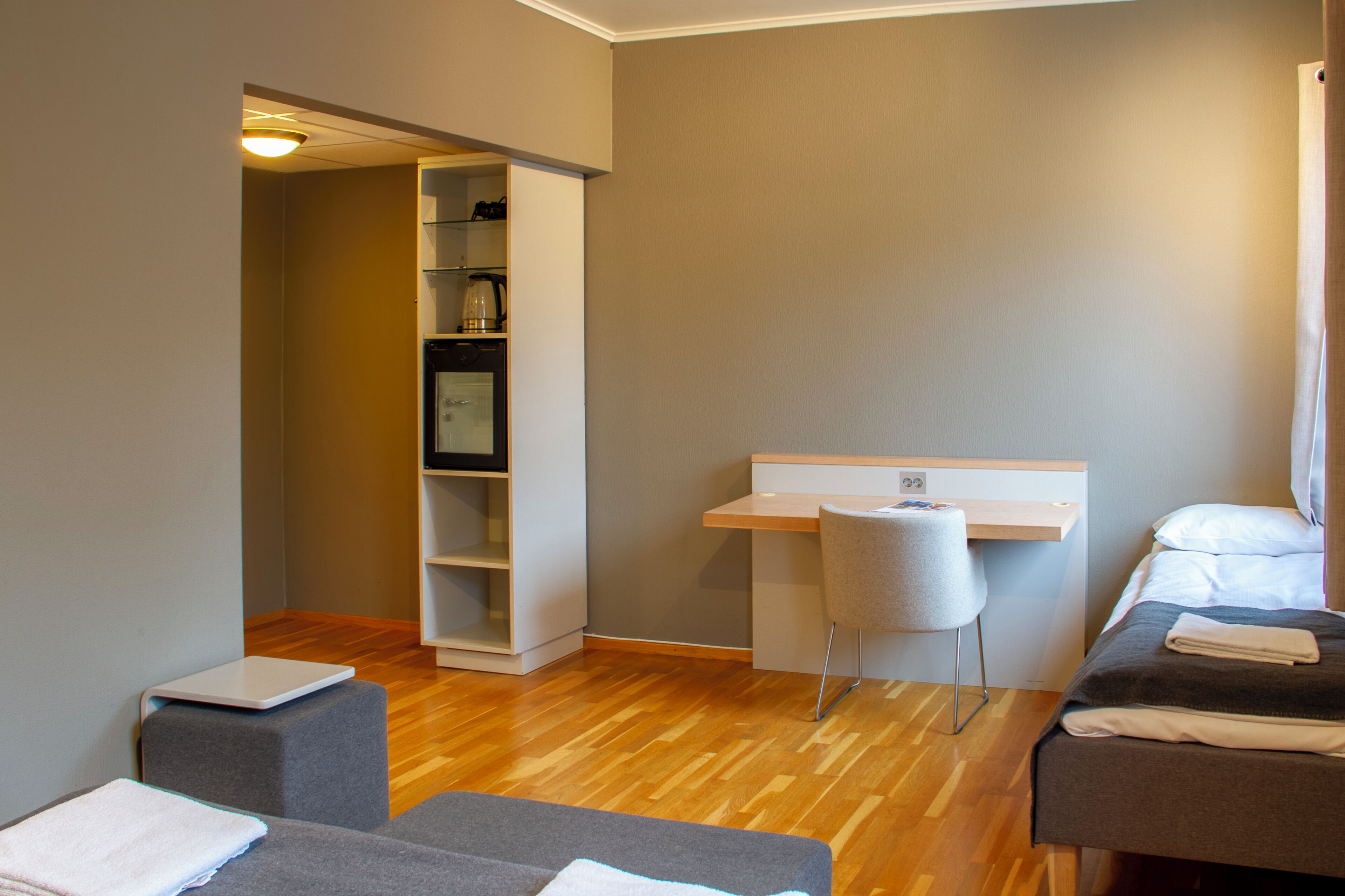 A hotel room with a bed, a desk, a chair, a small table, and a built-in shelf unit.