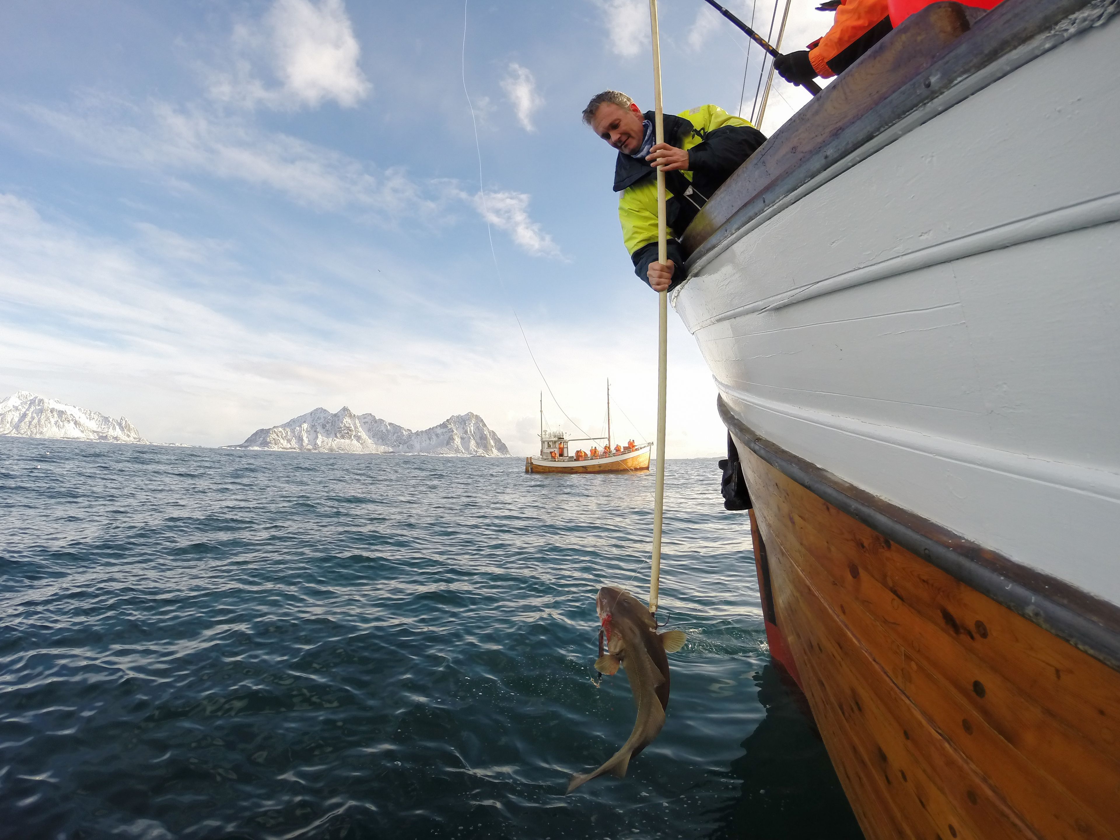 Pessoa num barco segurando uma vara de pesca com um peixe.