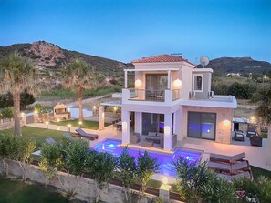 Ein modernes, zweistöckiges Haus mit Swimmingpool, Außensitzgelegenheiten und Blick auf die umliegenden Hügel.