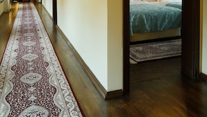 Un pasillo de hotel con alfombra roja, pisos de madera y una cama con ropa blanca en la habitación.