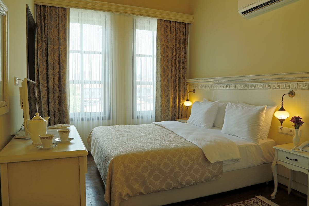 A neatly made bed with a patterned bedspread, a bedside table with a lamp, and a window with curtains.