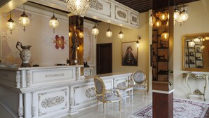 Un vestíbulo imponente con candelabros ornamentales, un mostrador de recepción de mármol y muebles clásicos.