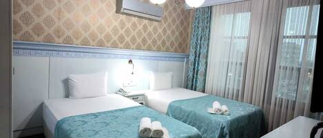 Habitación de hotel con dos camas, techo de madera, unidad de aire acondicionado, alfombra estampada y un pequeño escritorio con tetera.