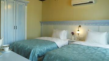 A hotel room with two beds, a wardrobe, a bedside table with a lamp, and an air conditioning unit.