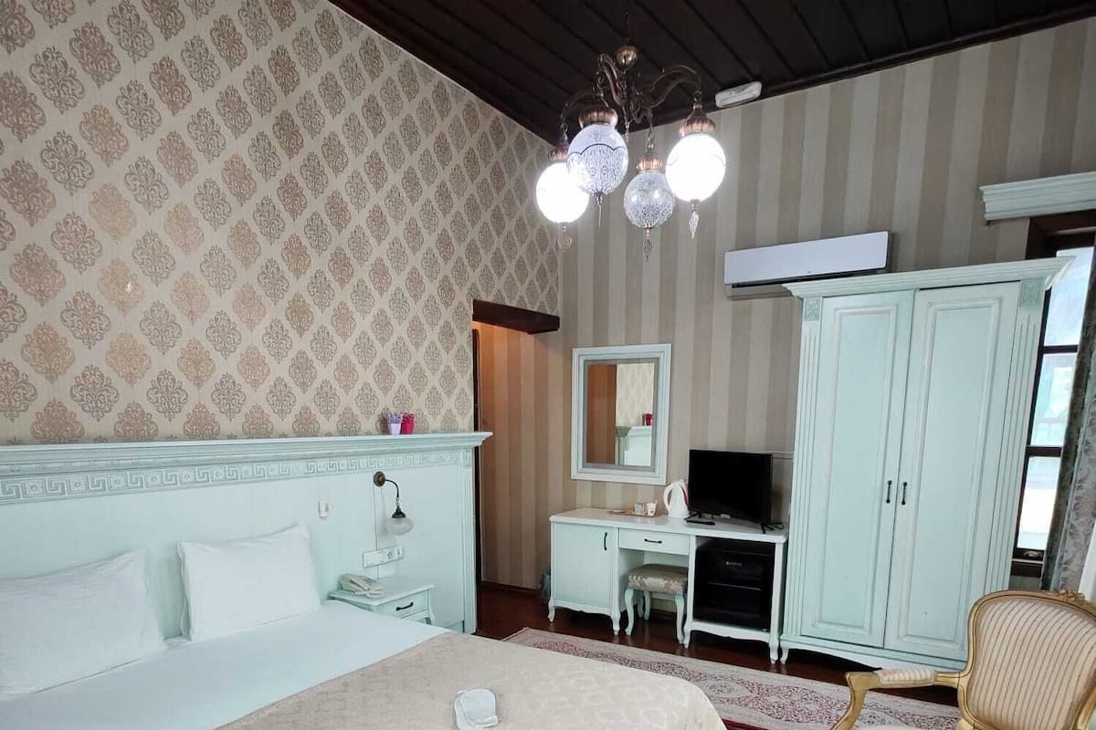 A hotel room with a large bed, a desk with a computer, a wardrobe, and two armchairs.