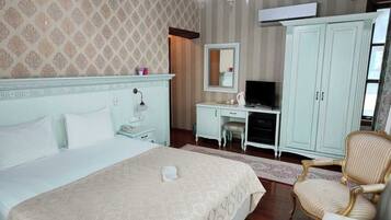 A hotel room with a large bed, a desk with a computer, a wardrobe, and two armchairs.