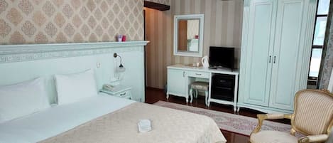 A hotel room with a large bed, a desk with a computer, a wardrobe, and two armchairs.