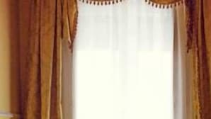 A vintage clawfoot bathtub with a wooden floor, curtains, and a window with sheer curtains.
