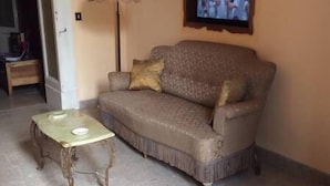 A living room with a sofa, a small table, a television mounted on the wall, and a lamp.