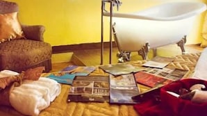 A room with a bathtub, a wooden floor, and a bed with a patterned headboard.