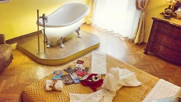 A room with a wooden floor, a bathtub, a bed with a patterned bedspread, and a dresser.