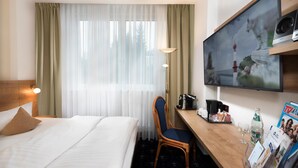 Habitación de hotel con cama, escritorio, silla, televisor y un mueble para revistas.