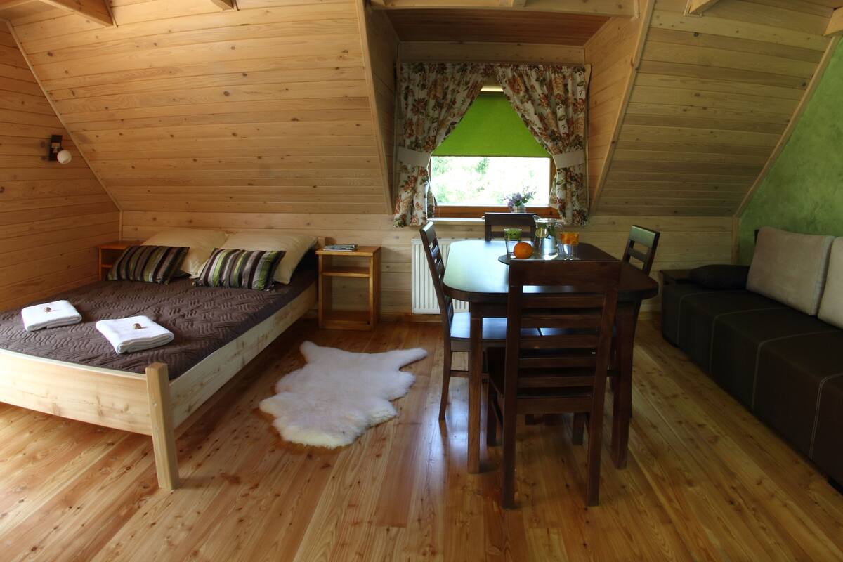 A cozy cabin interior with a bed, a dining table, and a sofa.