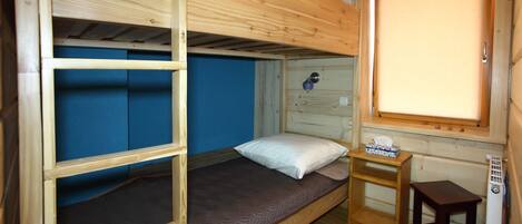 A compact wooden room with bunk beds, a small table, and a window with blinds.