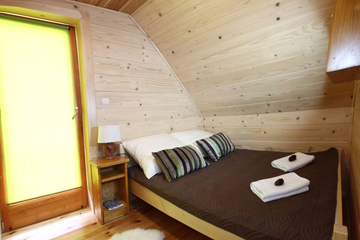 A wooden room with a bed, pillows, a nightstand, a lamp, and a fur rug.