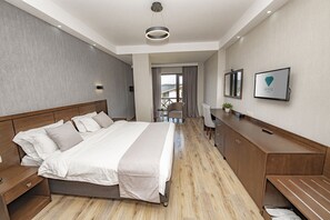 A modern hotel room with a large bed, wooden floor, a desk with a chair, a TV, and a view of the outdoors. - Hotel and SPA Crystal (Borjomi)