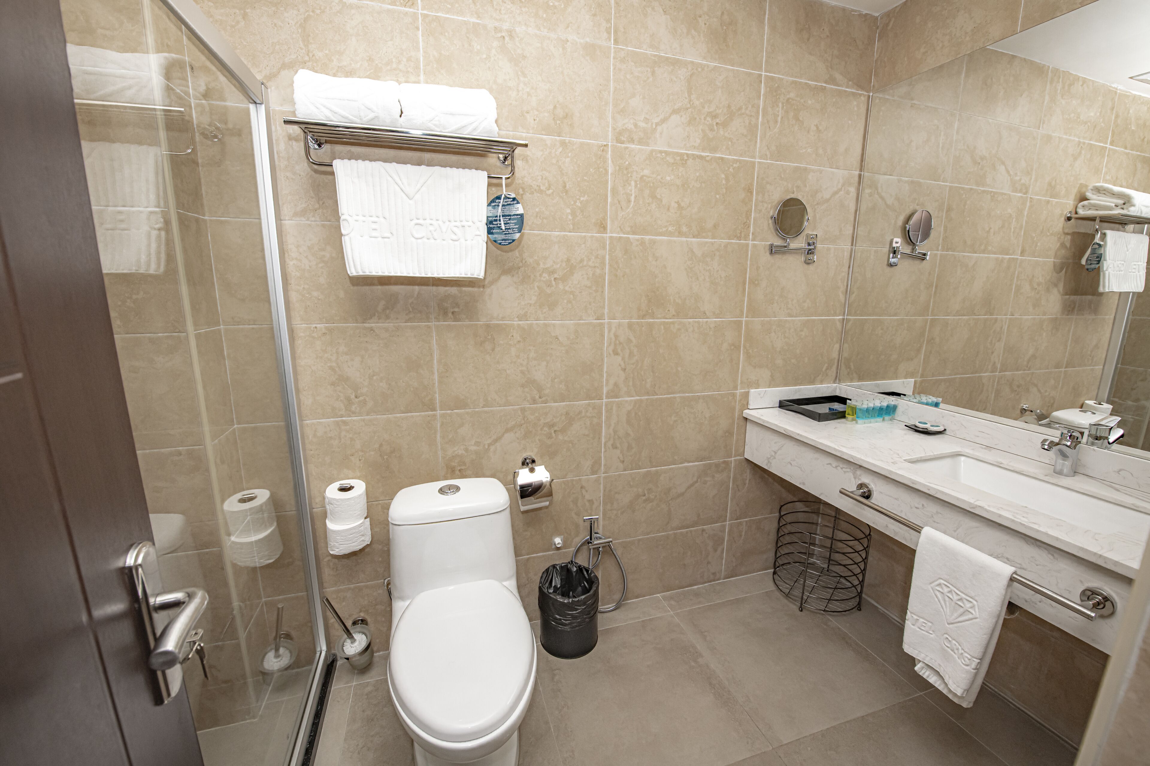 Un baño moderno con cabina de ducha de vidrio, inodoro, lavamanos con espejo y un perchero para toallas.
