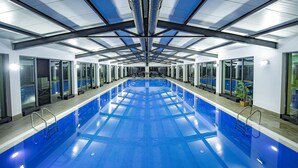 Une piscine intérieure moderne, dotée d’un plafond haut et de murs en verre.