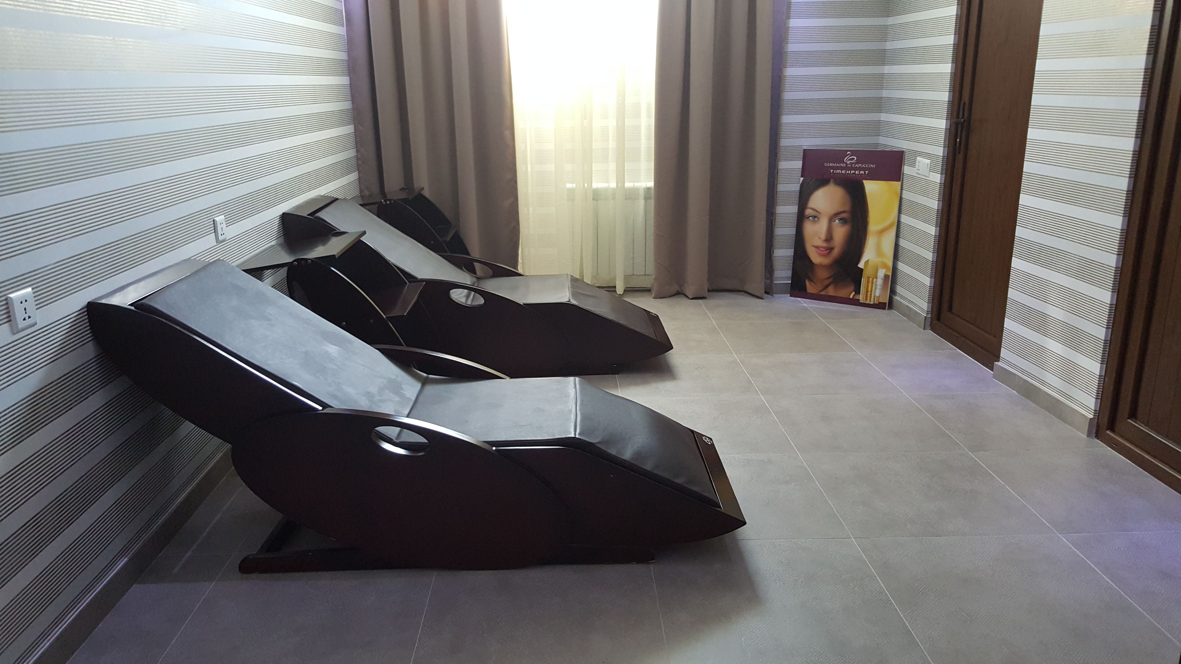 Un spa moderno con camillas de masaje negras, un ventanal con cortinas y un cartel en la pared.