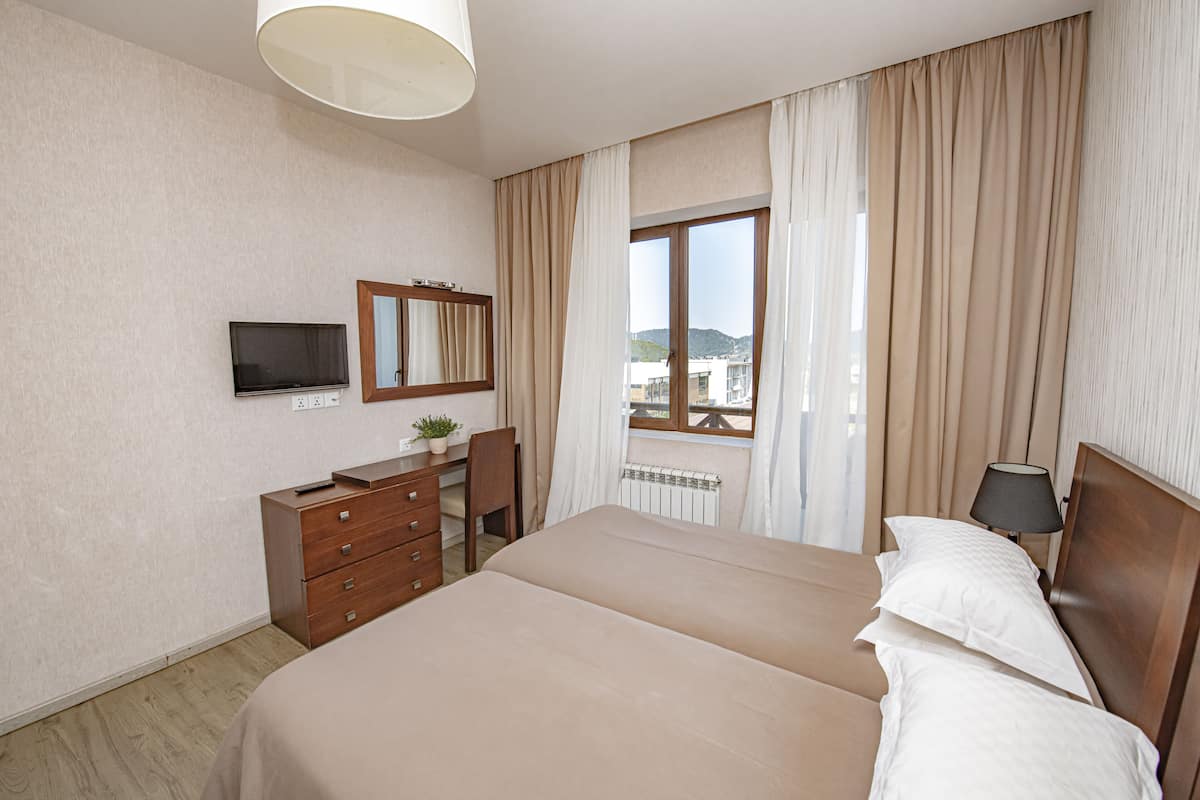 Une chambre d’hôtel avec un grand lit, un bureau avec une chaise, une télévision et une fenêtre avec des rideaux.