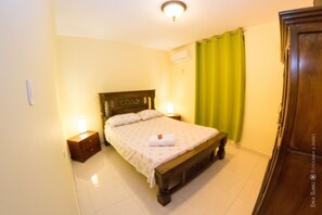 A bedroom with a wooden bed, two bedside tables with lamps, a green curtain, and a wooden wardrobe. - Apartamentos Villas de Cartagena (Cartagena)