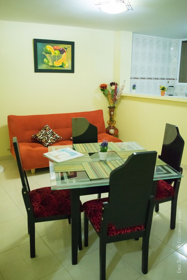 A dining area with a glass table, red upholstered chairs, a red sofa, and a framed artwork on the wall.